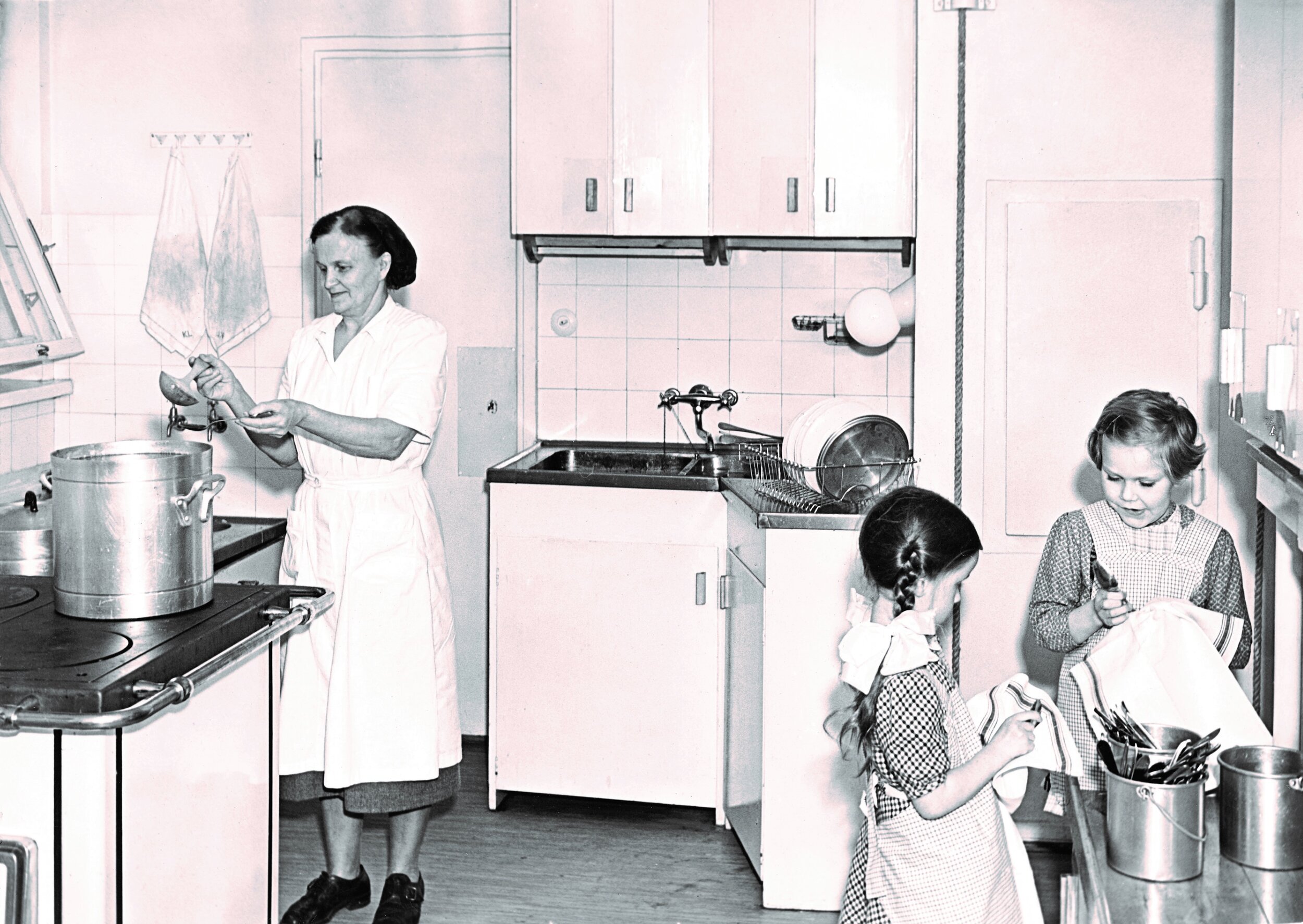 Kuva 2. Ryhmän lapset työskentelevät pöytien ääressä yhdessä huoneessa aikuisten valvonnan alla vuonna 1954. Kuva: Lastentarhamuseon kuvakokoelma.
