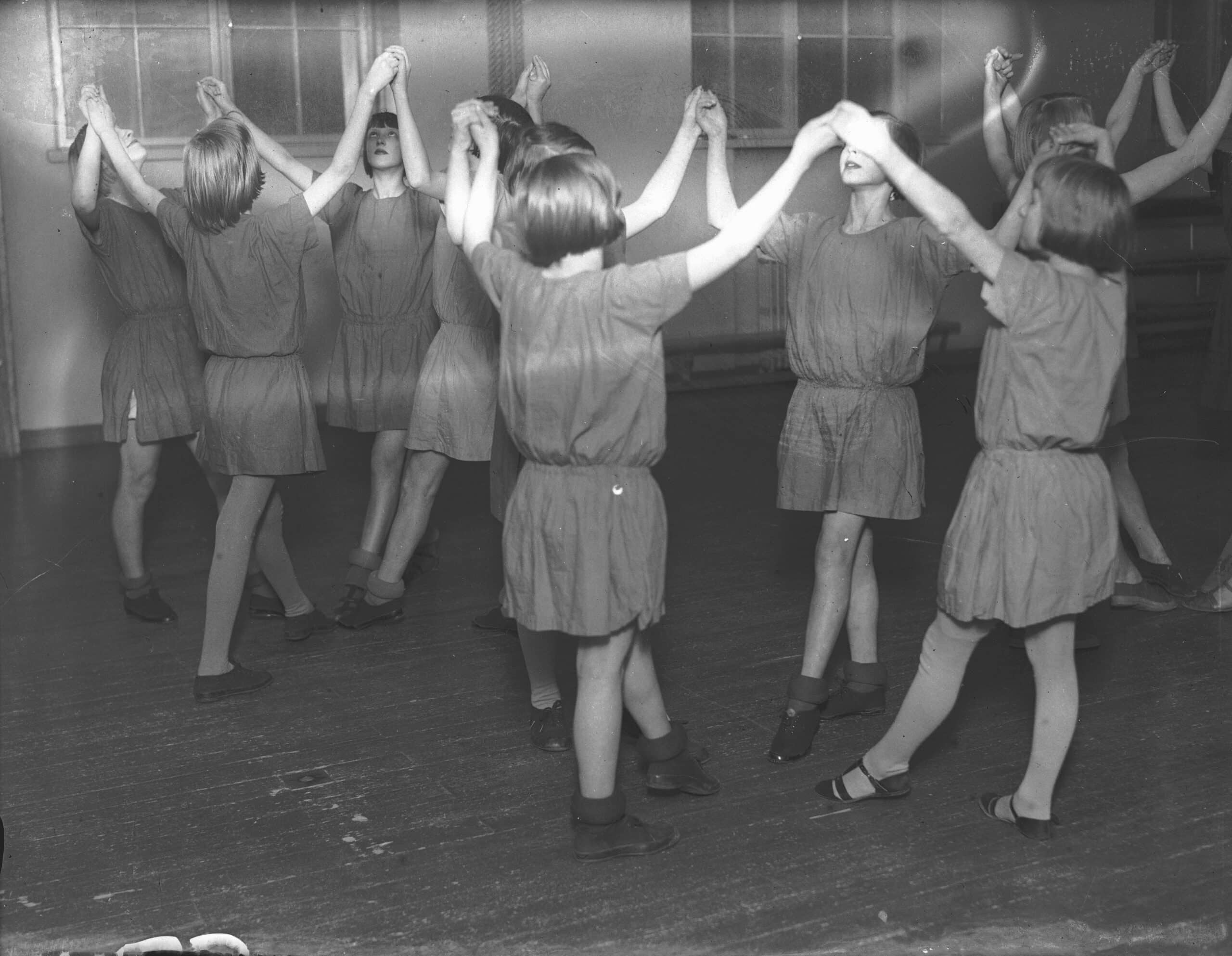 Yhdenmukaisiin asuihin pukeutuneet tytöt voimistelevat ryhmänä sisätiloissa Turussa 1930-luvulla.
