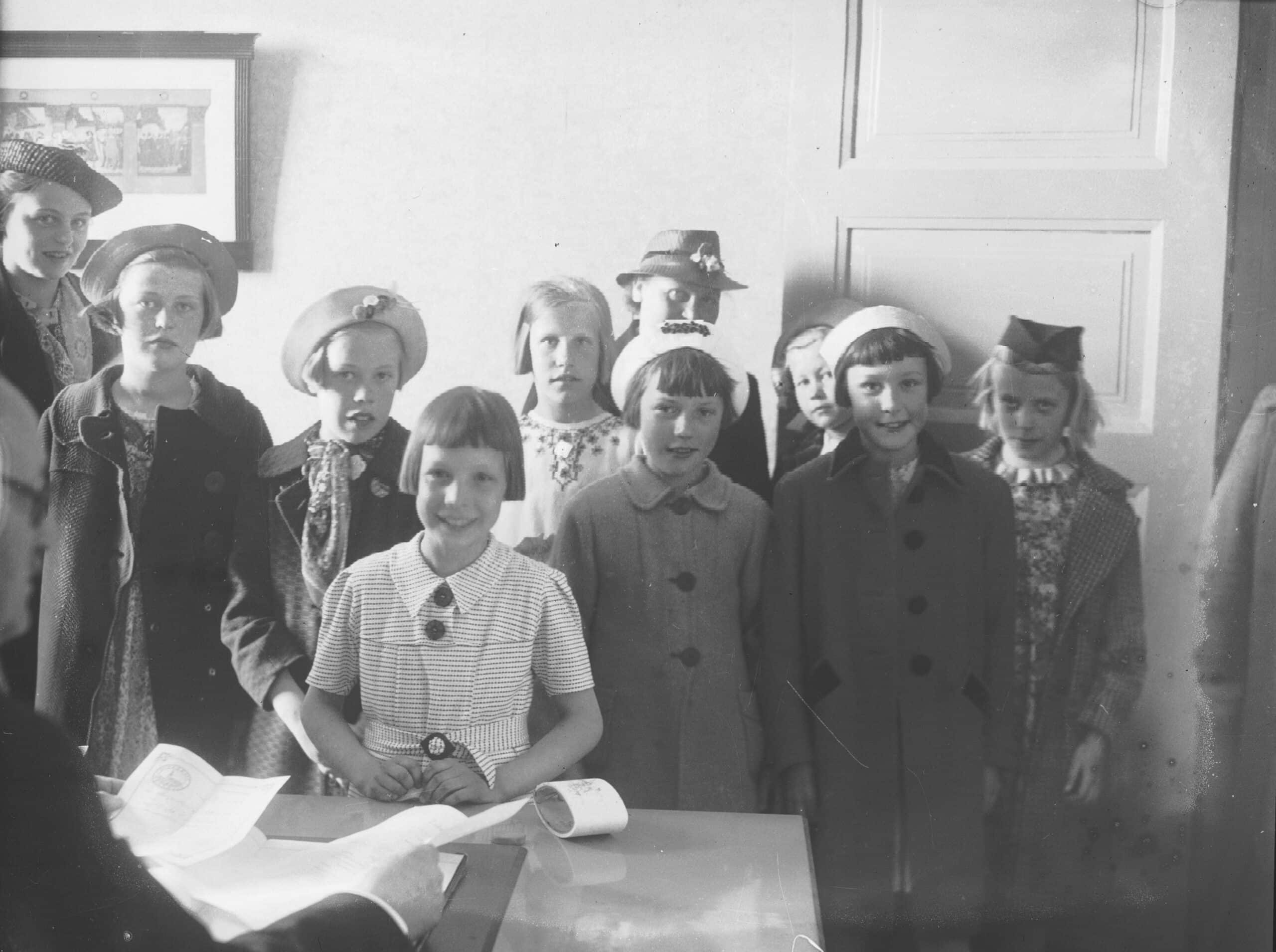 Ryhmä tyttöjä seisoo opettajan pöydän ääressä koulussa Turussa 1930-luvulla.